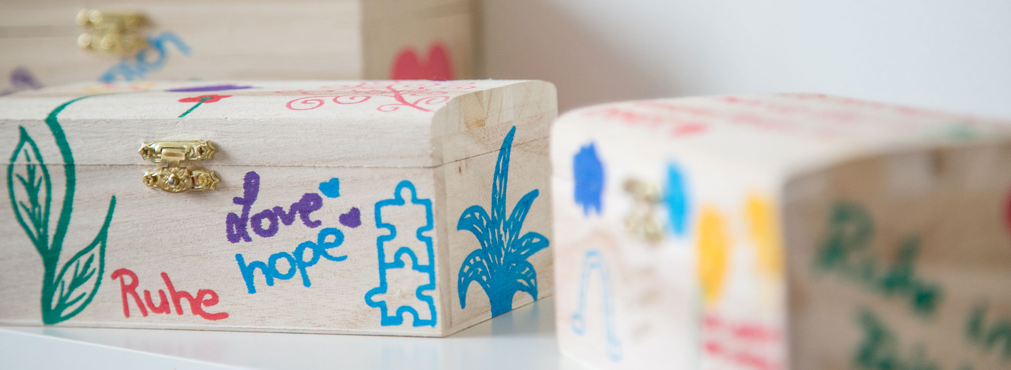 Kleine Holzkisten mit liebevollen, handgemalten Motiven und Wörtern wie „Ruhe“, „Liebe“ und „Hoffnung“.