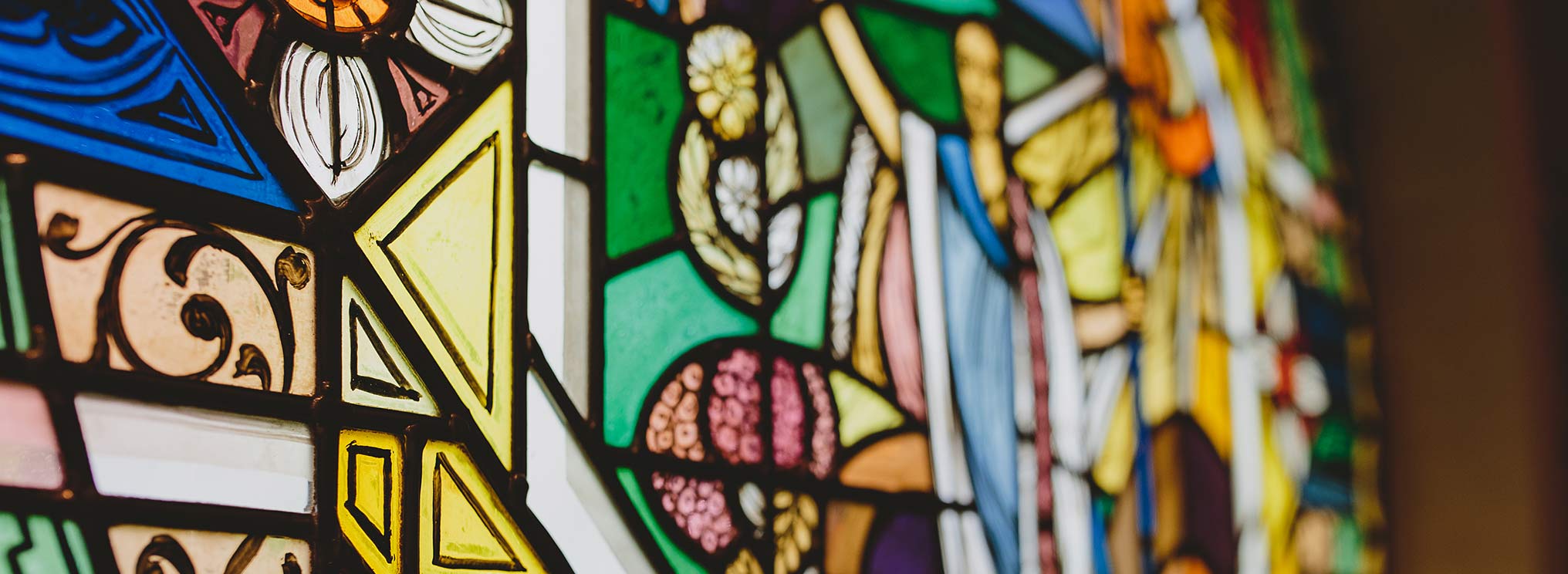 Detailaufnahme eines bunten, kunstvoll gestalteten Kirchenfensters mit floralen und geometrischen Mustern.