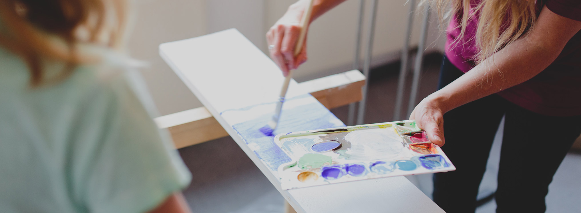 Eine Person bemalt liebevoll ein Abschiedsschild mit blauen und weißen Farben.