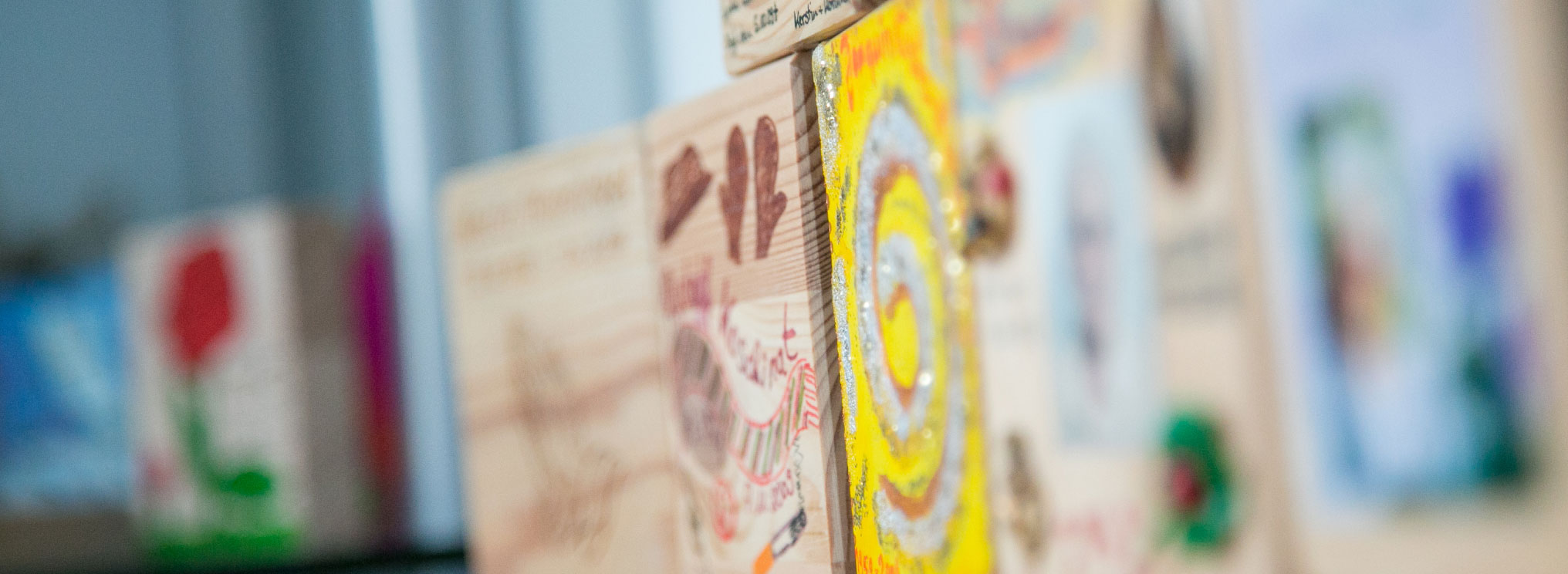 Nahaufnahme: Ein von Hand bemaltes Holzstück mit Erinnerungsmotiv zeigt gelb-rotes Muster.